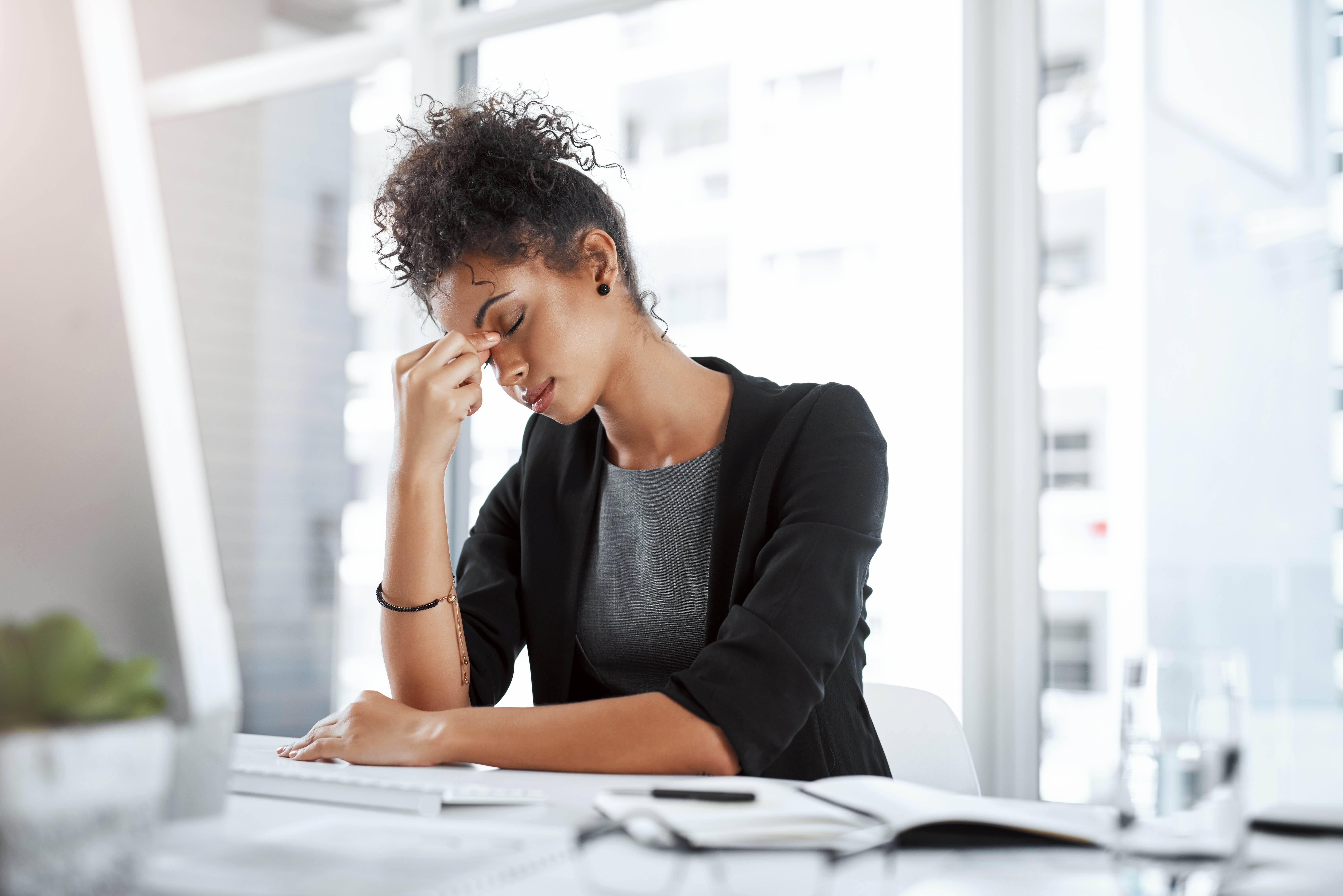 Woman sitting at her desk with her hand on her head, experiencing a headache during the workday